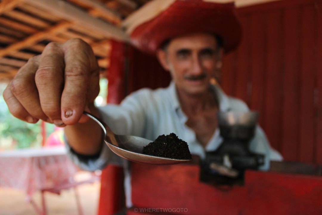 Man in a red beret holding out a spoon across a wooden counter in Vinales, Cuba
