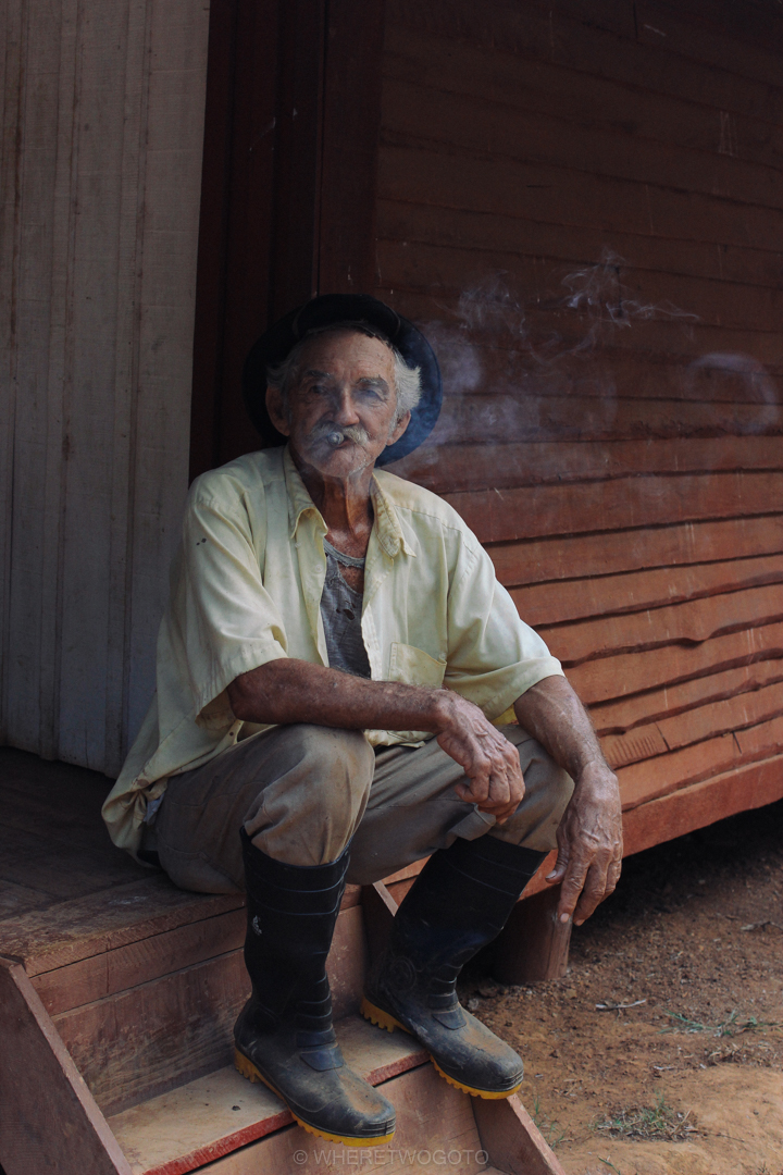 Elderly man in a hat smoking a cigar in the doorway of a wooden house in Vinales, Cuba